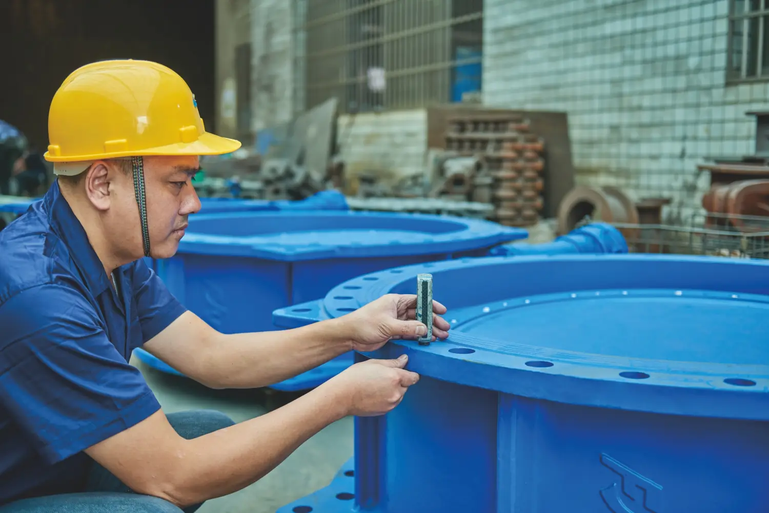 worker inspecting large blue valve component